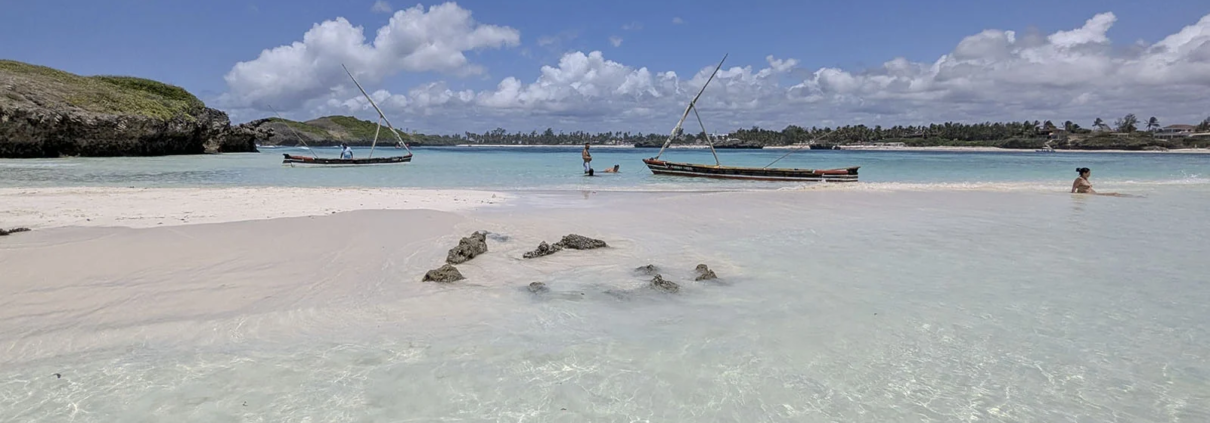 Traditional wooden boats in shallow turquoise water on a beach in Watamu, Kenya.