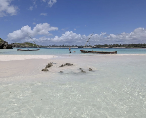 Traditional wooden boats in shallow turquoise water on a beach in Watamu, Kenya.